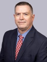 Photo of James Roundtree wearing a jacket and tie.